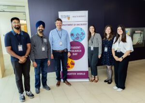 Five people standing beside a free-standing banner for the department of Oncology Student Research Day