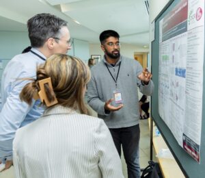 Three people standing in front of a poster board with one person looking at the poster and pointing